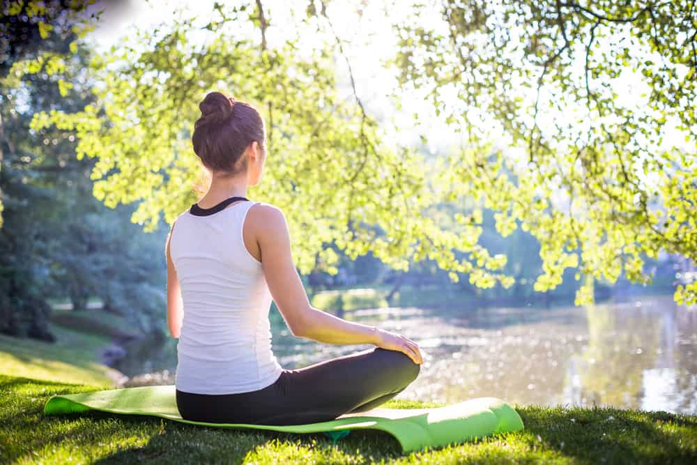 איך להתחיל לתרגל מדיטציה עוד היום! Young woman doing yoga in morning park near lake