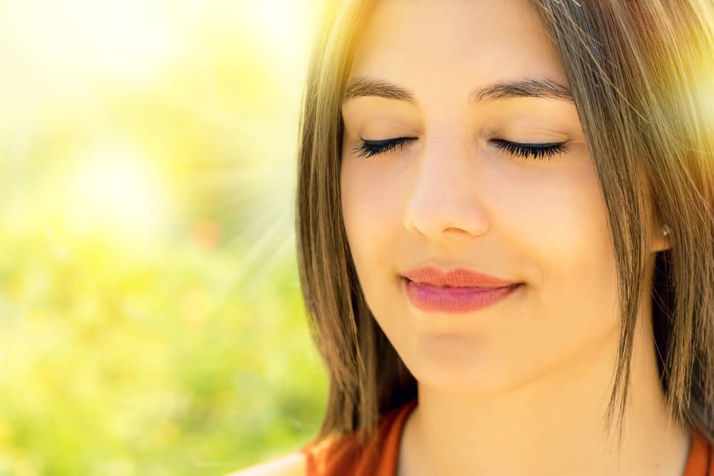 איך לפתח שיח פנימי חיובי? Face shot of relaxed woman meditating outdoors.